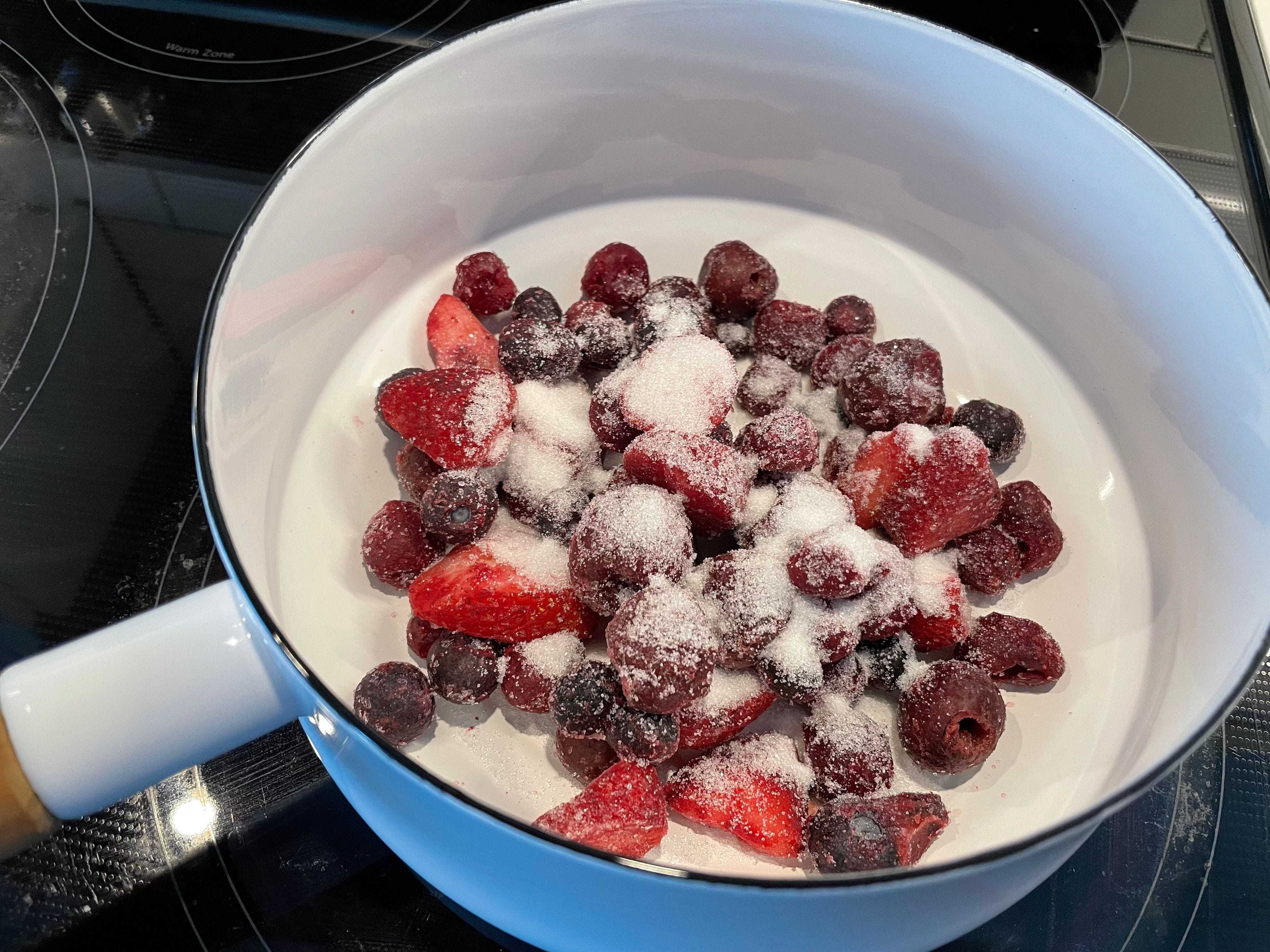 Add frozen fruit to a saucepan with sugar.