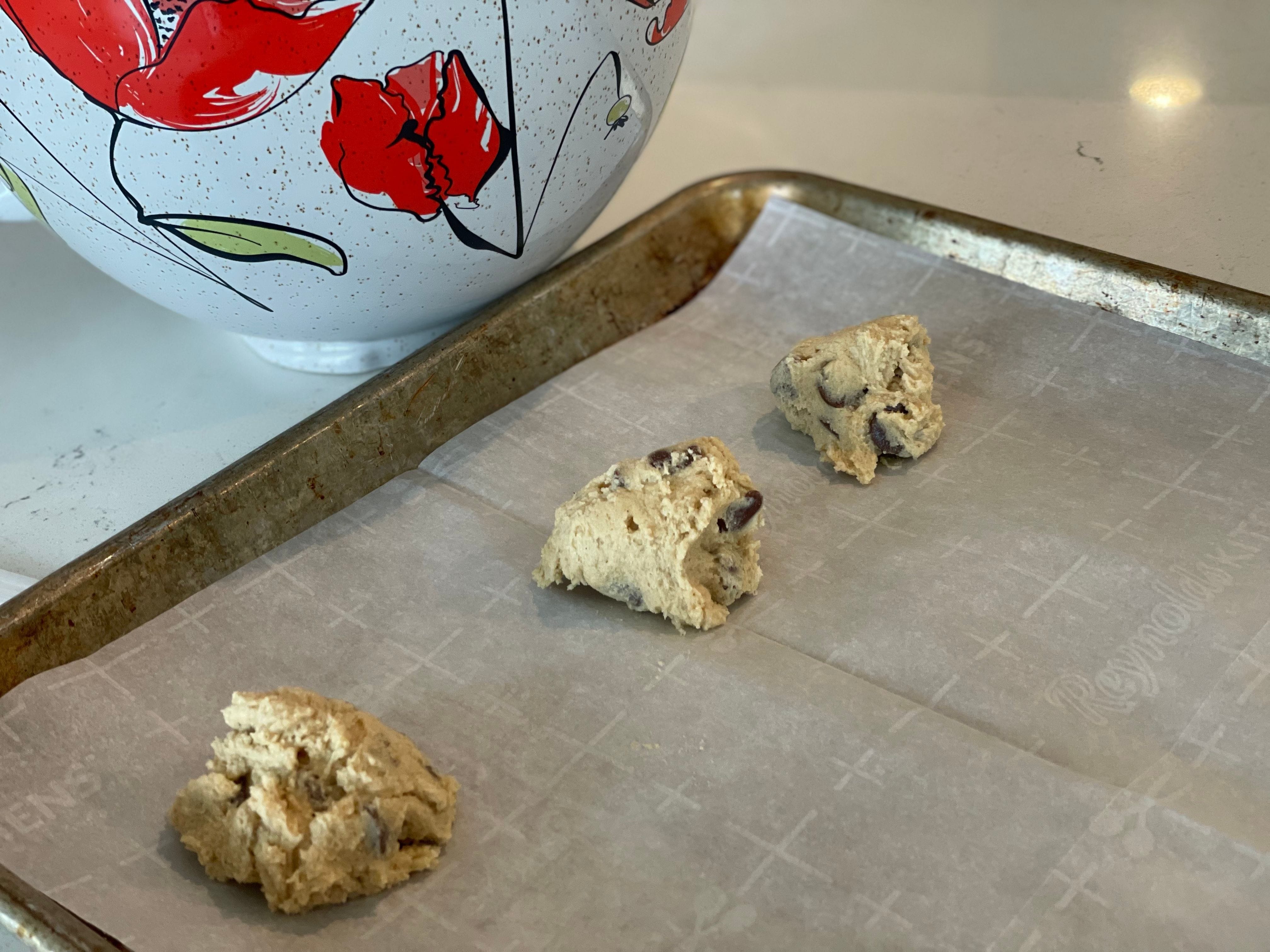 Mounds of raw chocolate chip cookie dough on a baking sheet.